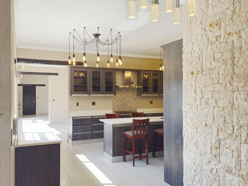 Modern kitchen featuring a stone-clad feature wall, central island, dark cabinetry, and contemporary pendant lighting, finished with clean tiled flooring.