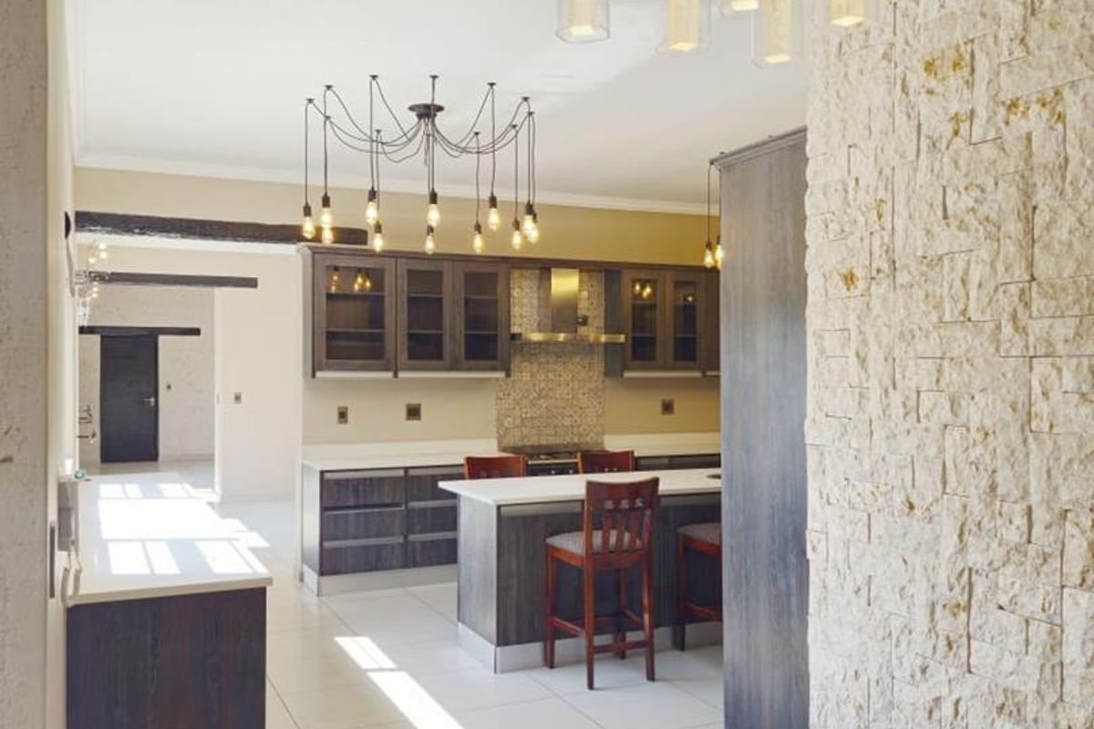 Modern kitchen featuring a stone-clad feature wall, central island, dark cabinetry, and contemporary pendant lighting, finished with clean tiled flooring.