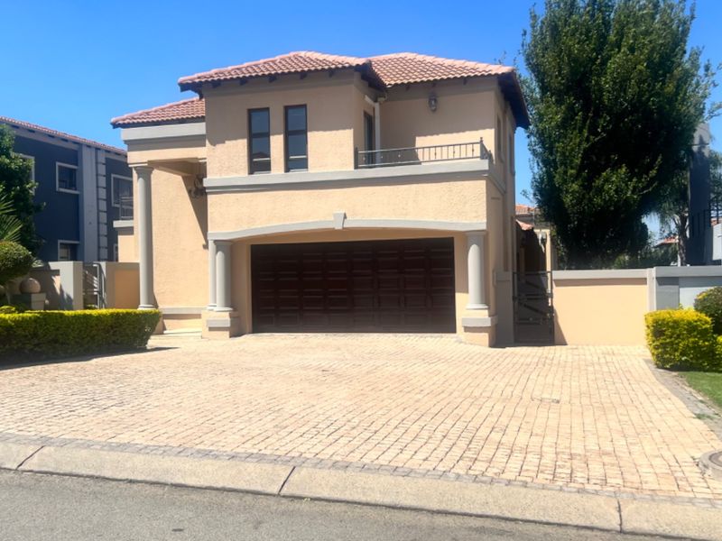 Front elevation of a double-story house featuring a paved driveway, double garage, and an upper-level balcony with decorative architectural columns.