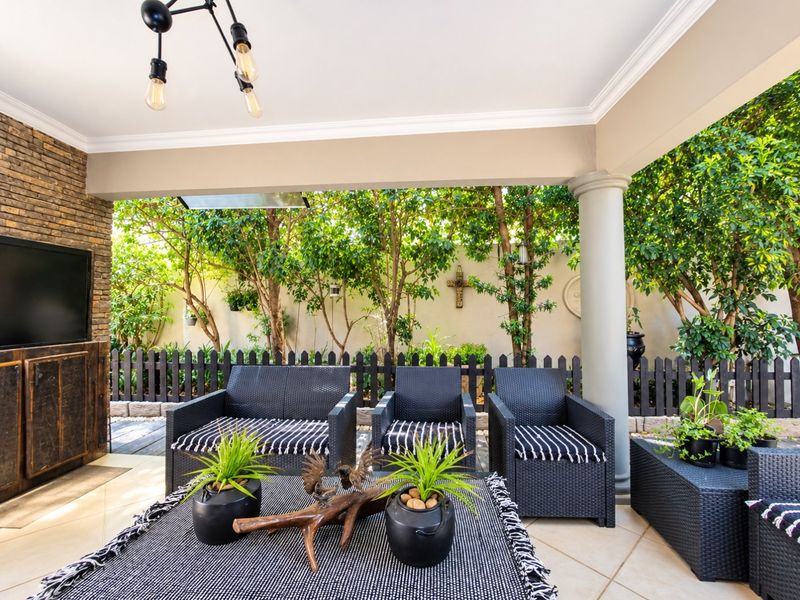 A well-maintained covered patio featuring tiled flooring, a stone-clad feature wall, and a decorative column, overlooking a private garden with a picket fence.
