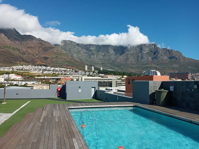 Rooftop swimming pool area featuring timber decking, artificial grass, and panoramic mountain views.