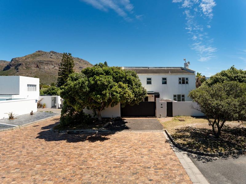 Front exterior view of a two-story residential property featuring a paved driveway, boundary wall, and gated entrance set against a mountain backdrop.