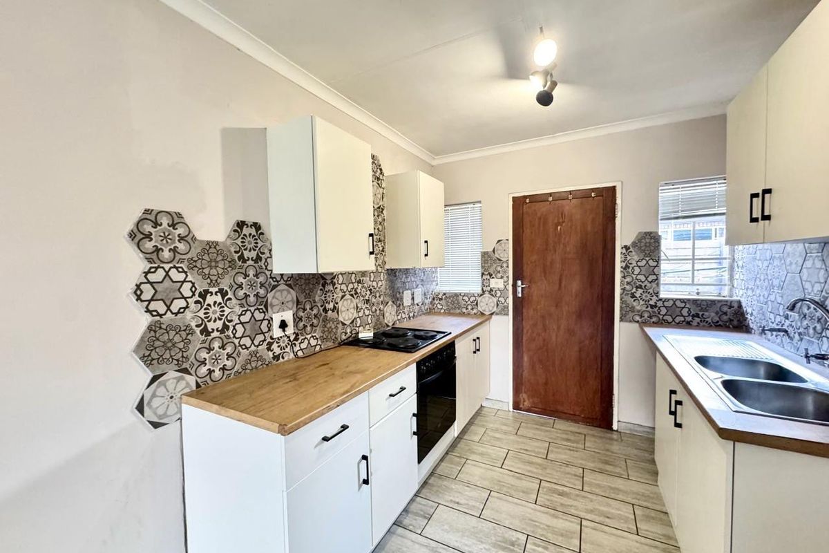 A functional kitchen featuring white cabinetry, wood-look countertops, a built-in oven and hob, and decorative patterned tile splashbacks.