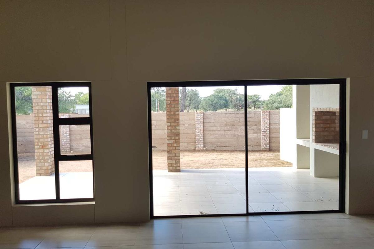 Interior view looking out through large sliding glass doors onto a covered patio area with a built-in brick braai and garden view.