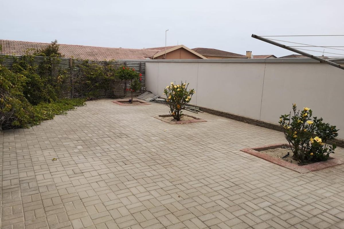 A paved rear courtyard area featuring a boundary wall, established garden beds, and a clothesline.