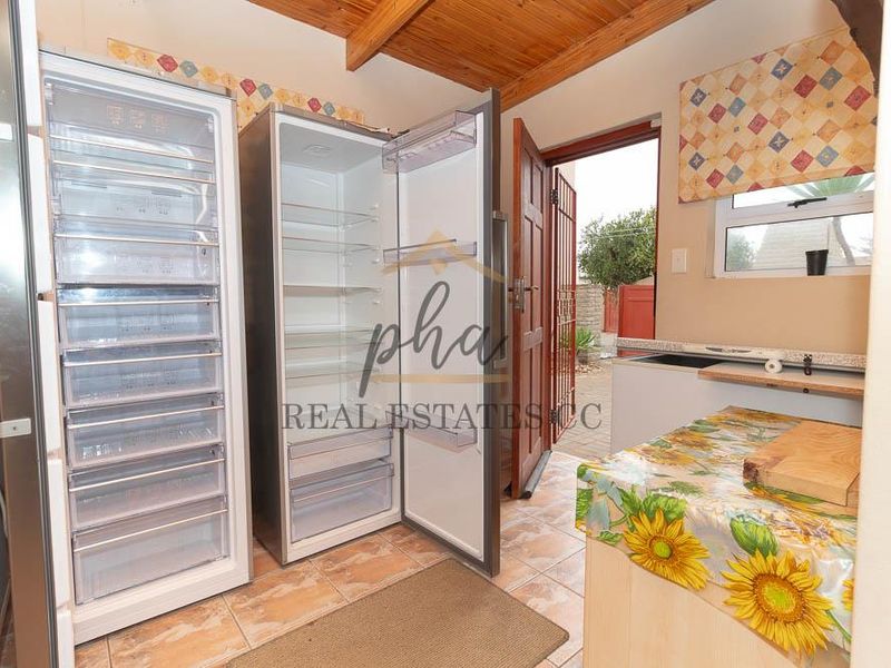 A functional scullery or utility area featuring tiled flooring, exposed timber ceiling beams, and direct access to the exterior.