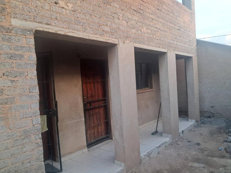 Rear exterior view of a property featuring a covered patio with tiled flooring, concrete pillars, and security gates, currently in an unfinished construction state.