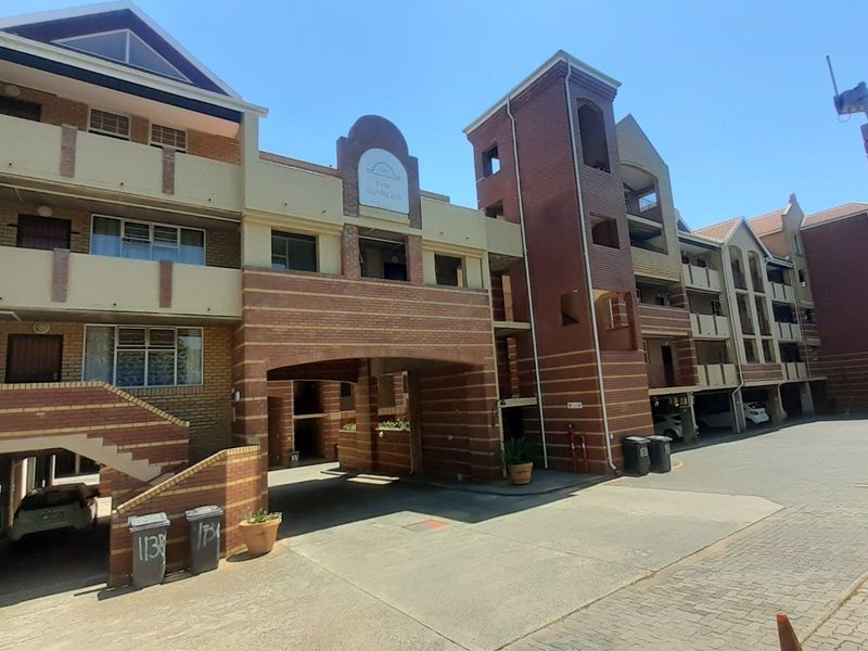 Front elevation of The Gables apartment complex, featuring multi-story brick architecture, covered parking areas, and external staircases.
