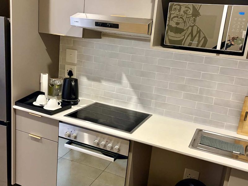 Modern kitchen featuring sleek cabinetry, stone countertops, subway tile backsplash, integrated oven, electric hob, and a stylish brass faucet.