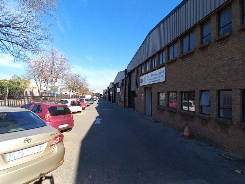 Exterior view of an industrial warehouse complex featuring brick facade, metal roofing, and paved driveway access with parking.