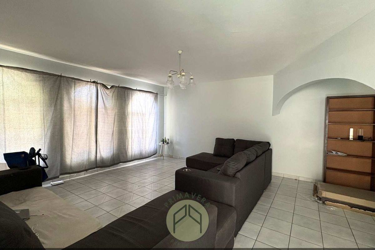 Spacious living room featuring neutral tiled flooring, an arched wall detail, and large windows allowing for ample natural light.