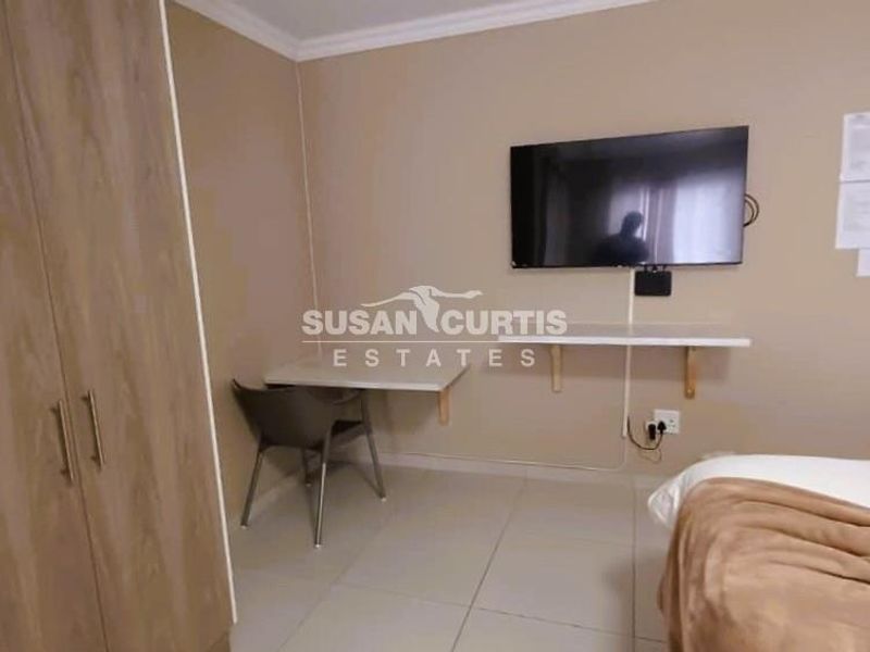 A functional bedroom featuring a built-in wardrobe, wall-mounted desk, and tiled flooring, providing a practical space for guests.