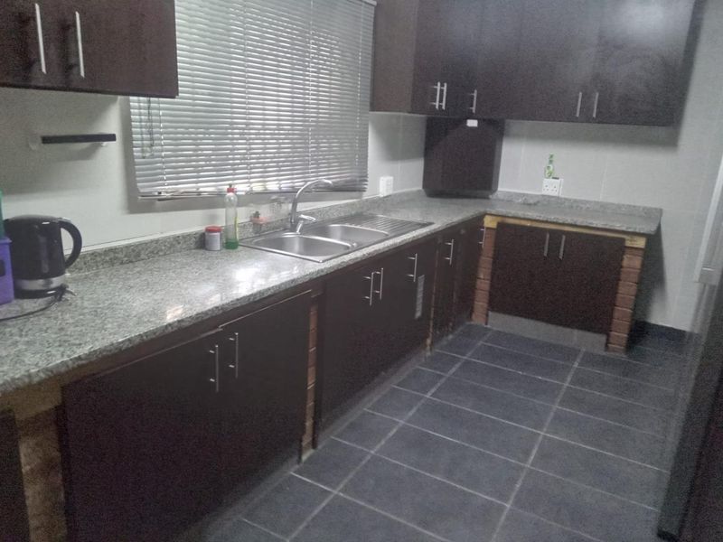 A functional kitchen featuring dark wood cabinetry, granite countertops, a stainless steel double sink, and tiled flooring with some unfinished base detailing.