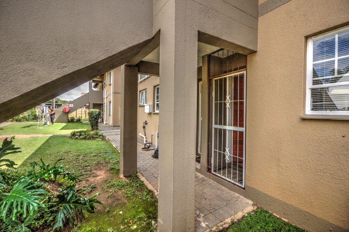 Exterior view of the townhouse ground floor entrance featuring a covered walkway, security gate, and access to the communal garden area.