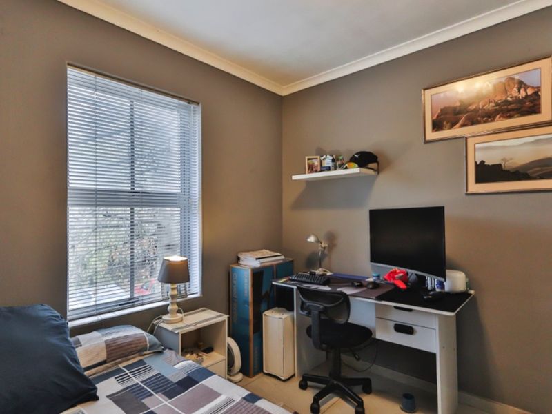 A functional bedroom featuring neutral wall tones, a window with venetian blinds, and a built-in floating shelf, offering a versatile space for rest or study.