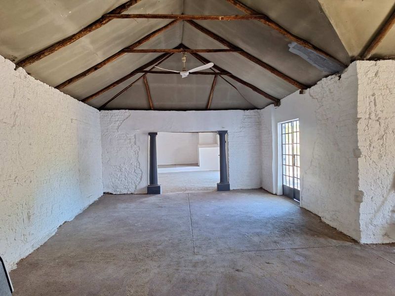 An expansive, empty living area featuring a high vaulted ceiling with exposed timber trusses, textured white walls, and durable concrete flooring.