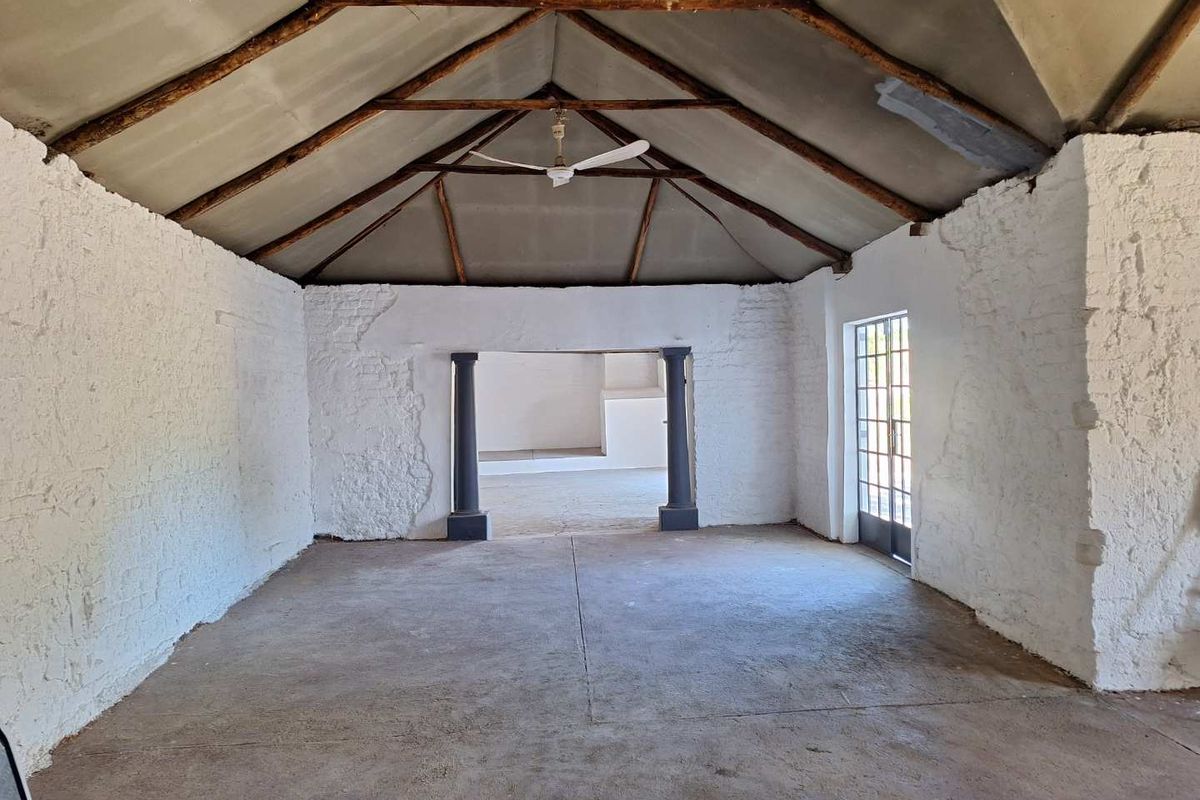 An expansive, empty living area featuring a high vaulted ceiling with exposed timber trusses, textured white walls, and durable concrete flooring.