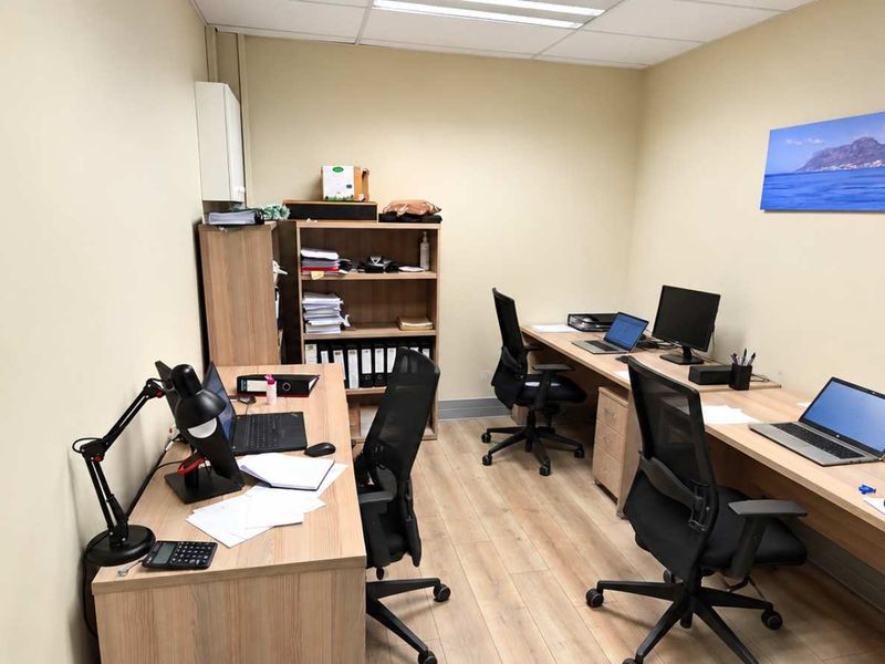 A functional office space featuring laminate flooring, a suspended ceiling with recessed lighting, and built-in desk configurations.