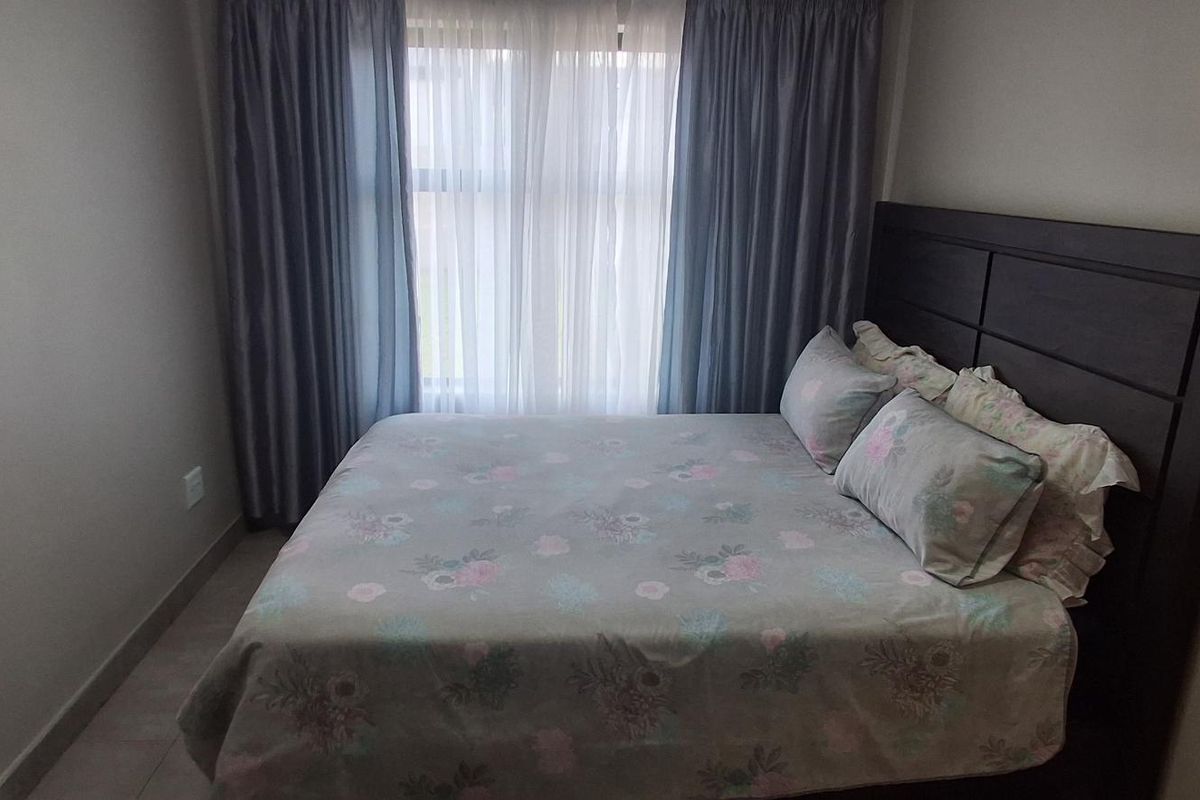 A well-maintained bedroom featuring neutral wall tones, tiled flooring, and a large window dressed with floor-to-ceiling curtains.