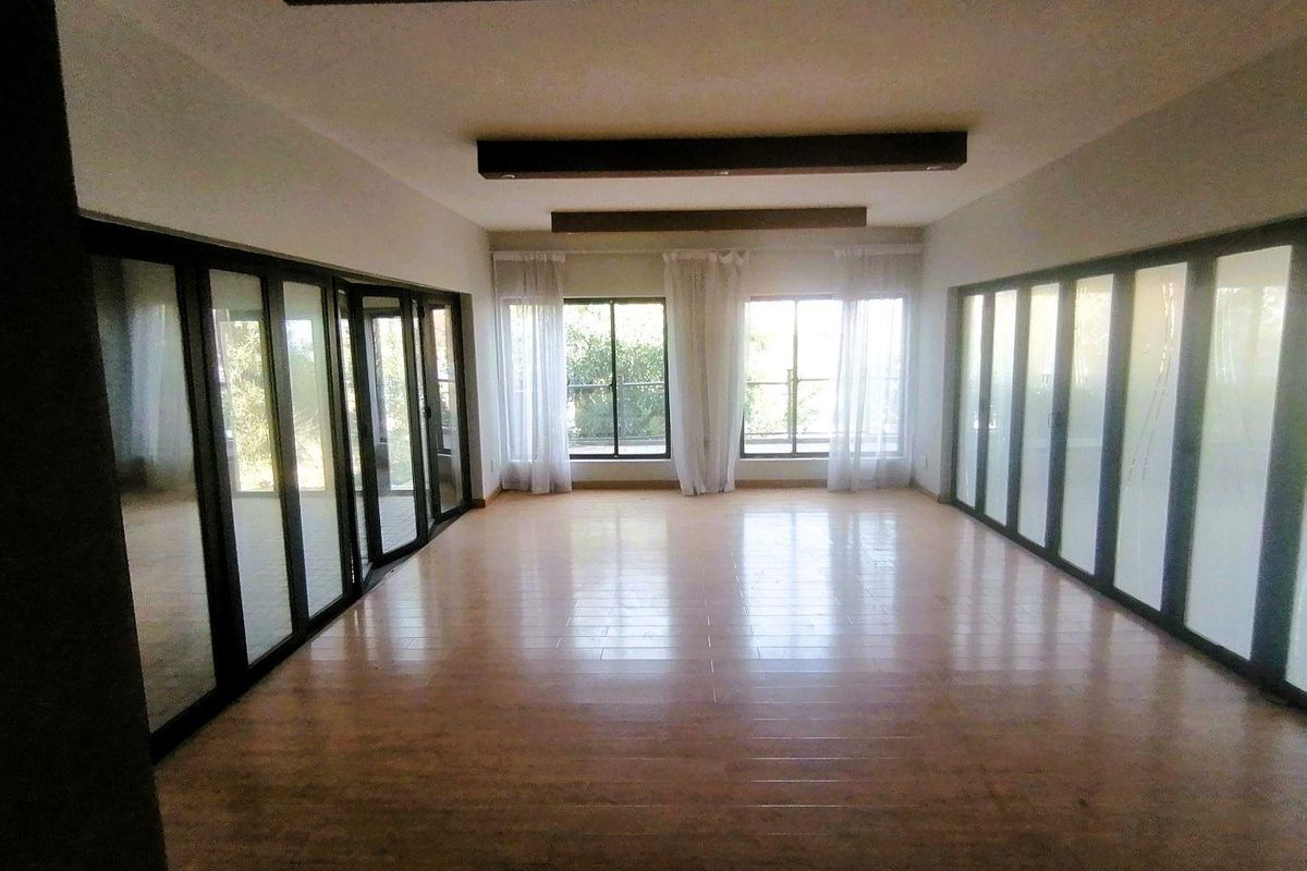 Spacious, empty living area featuring modern laminate flooring, recessed ceiling beams with downlights, and extensive glass sliding doors providing ample natural light.