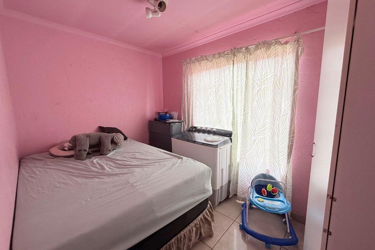 A bedroom featuring tiled flooring and a built-in wardrobe, currently utilized with a washing machine placed near the window.