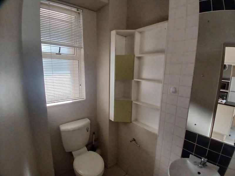 A compact bathroom featuring a standard toilet, wall-mounted basin, and built-in shelving, requiring cosmetic updates to improve its dated appearance.
