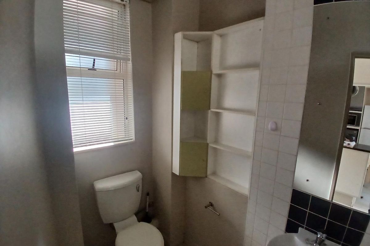A compact bathroom featuring a standard toilet, wall-mounted basin, and built-in shelving, requiring cosmetic updates to improve its dated appearance.