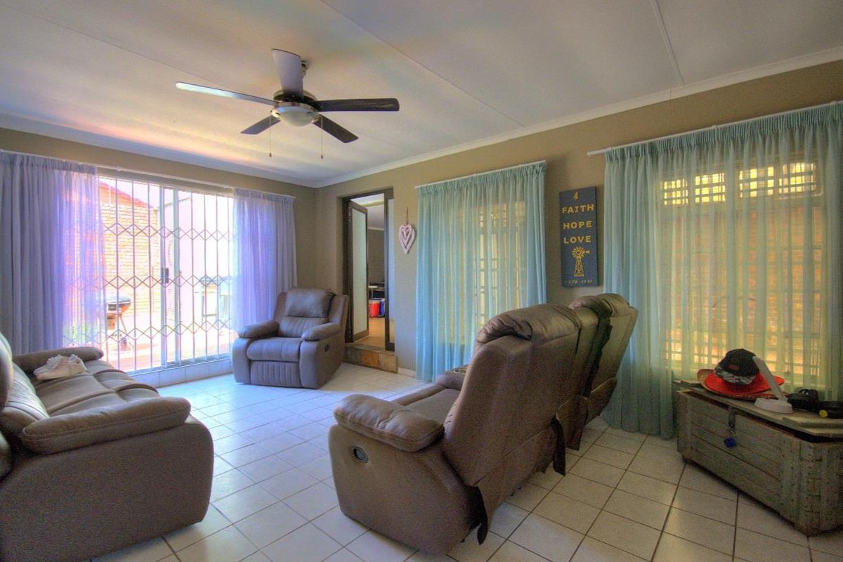 A living room featuring tiled flooring, a ceiling fan, and sliding glass doors with security gates leading to the exterior.