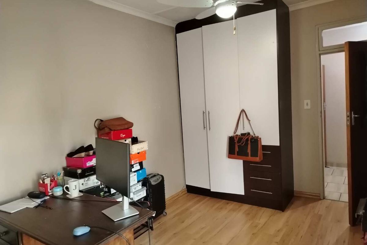 A bedroom featuring laminate flooring, a built-in wardrobe with a two-tone finish, and a ceiling fan.