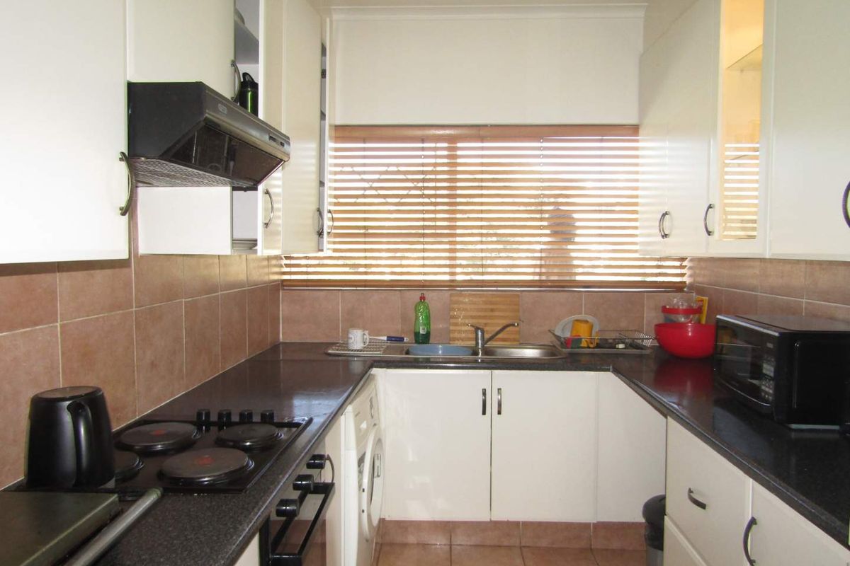 A functional galley-style kitchen featuring white cabinetry, dark countertops, tiled splashbacks, a built-in hob, and an integrated laundry appliance space.