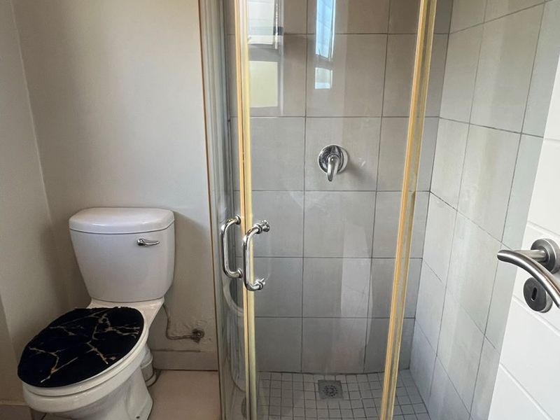 A functional bathroom featuring a corner shower enclosure with tiled walls and a standard toilet.