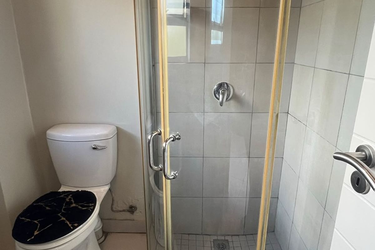 A functional bathroom featuring a corner shower enclosure with tiled walls and a standard toilet.