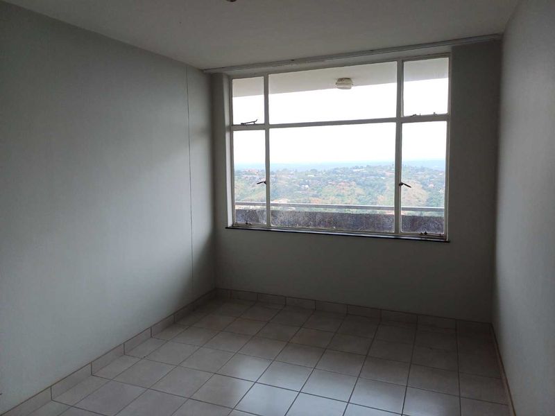 An empty bedroom featuring tiled flooring and a large window offering expansive elevated views, providing a blank canvas for personalization.