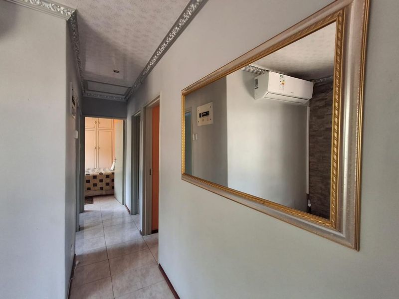A tiled hallway featuring decorative ceiling cornicing and a wall-mounted split-system air conditioning unit, providing access to adjacent rooms.