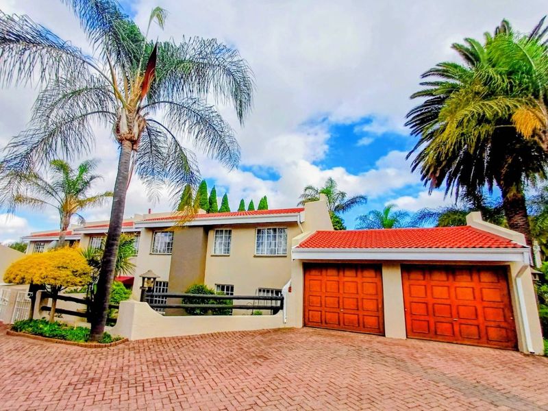 Front exterior view of a townhouse featuring a paved driveway, double wooden garage doors, and a tiled roof.