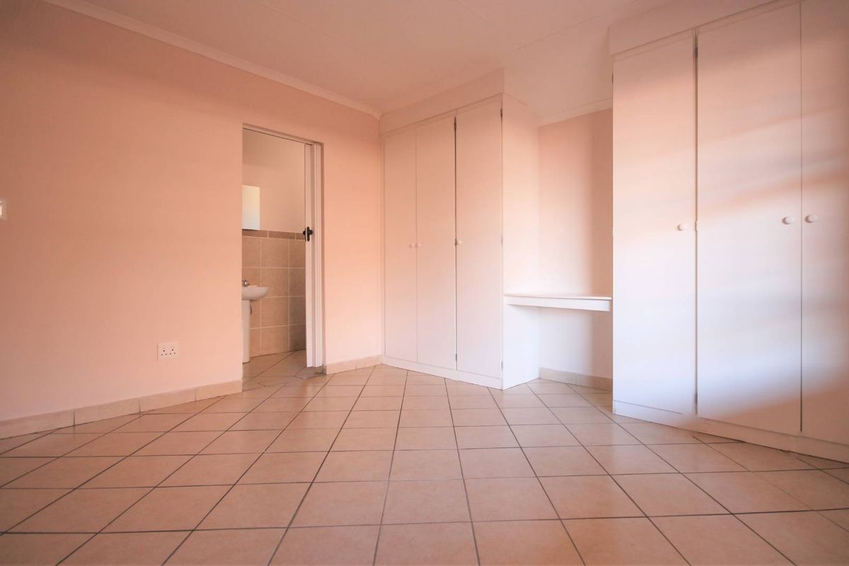 A spacious, empty bedroom featuring neutral tiled flooring, ample built-in cupboard storage, and direct access to an en-suite bathroom.