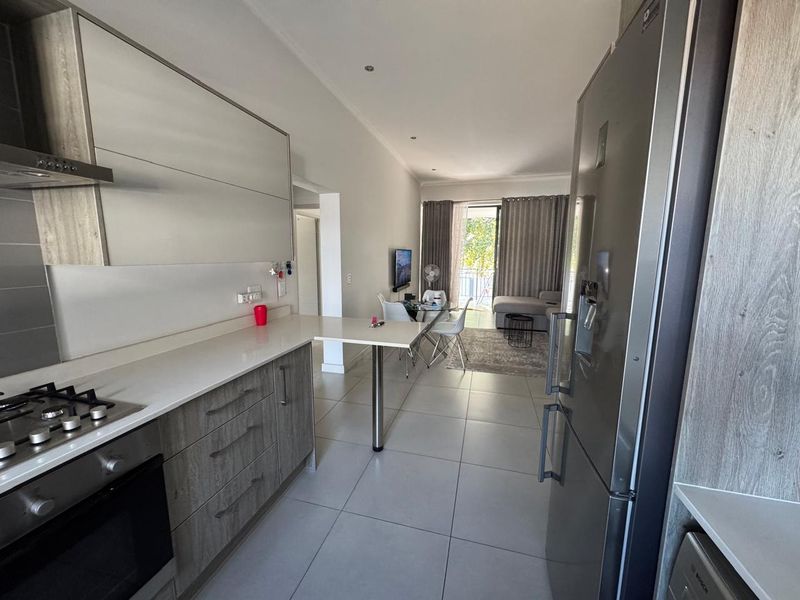 Modern open-plan kitchen and living area featuring sleek cabinetry, stone countertops, integrated appliances, and direct access to a balcony through sliding glass doors.