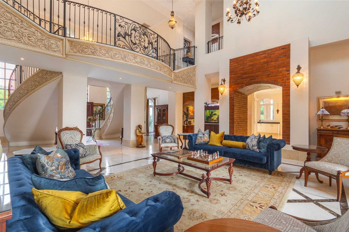 Grand double-volume living area featuring an ornate wrought-iron mezzanine balcony, exposed brick archway, and polished marble flooring with decorative inlay.