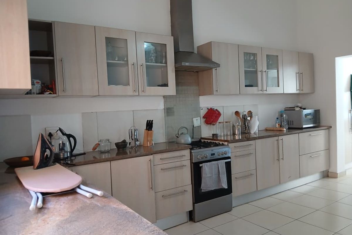 A functional kitchen featuring light wood-finish cabinetry, granite countertops, a stainless steel extractor fan, and a freestanding oven with a tiled splashback.