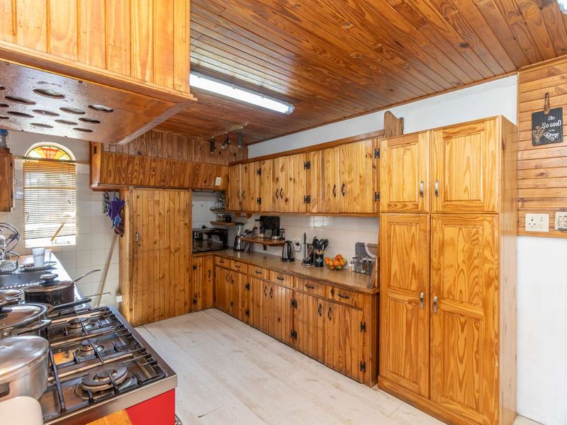 A traditional kitchen featuring extensive timber cabinetry, a timber-clad ceiling, a gas stove, and a double sink with tiled splashbacks.