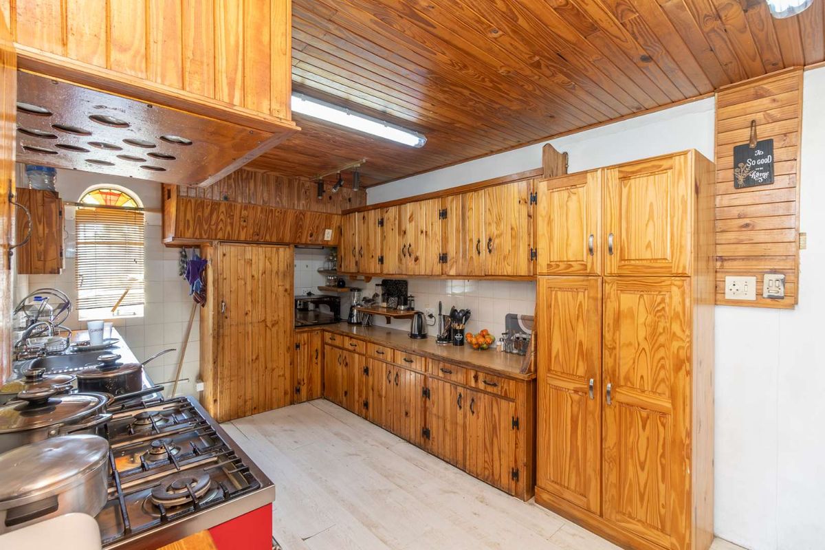 A traditional kitchen featuring extensive timber cabinetry, a timber-clad ceiling, a gas stove, and a double sink with tiled splashbacks.