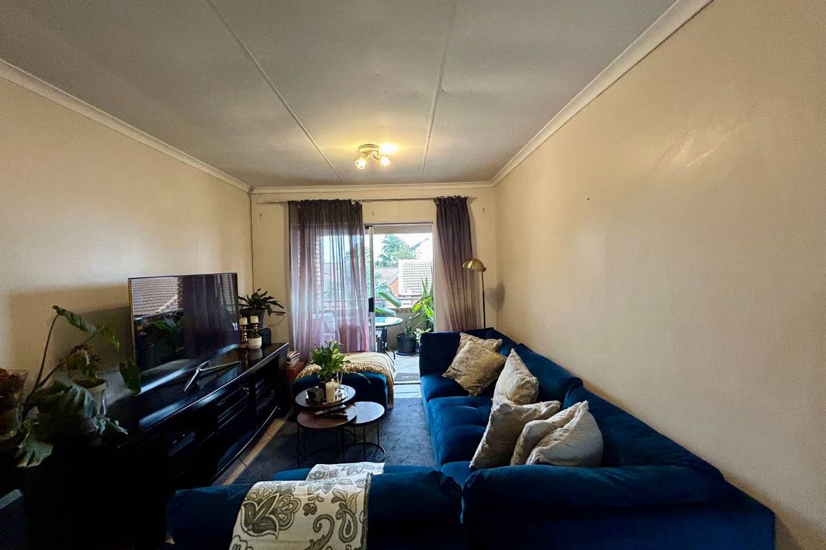 A cozy living room featuring a sliding glass door leading to a balcony, finished with standard ceiling cornicing and neutral wall paint.