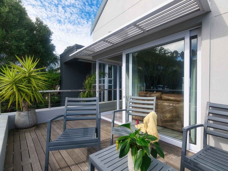 A well-maintained timber balcony featuring a fixed louvered awning, metal balustrade, and large sliding glass doors providing seamless indoor-outdoor flow.