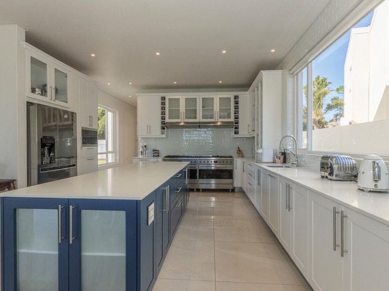 Modern, spacious kitchen featuring a large central island, quartz countertops, high-end stainless steel appliances, and ample built-in cabinetry with a clean, contemporary finish.