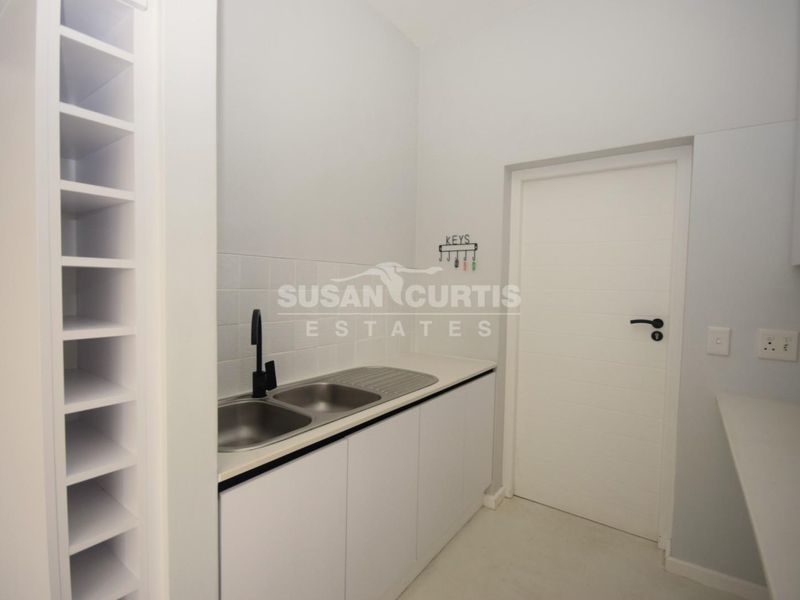 A clean and modern scullery featuring built-in cabinetry, a double stainless steel sink with a black mixer tap, and ample storage shelving.