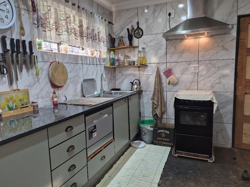 A functional kitchen featuring granite countertops, tiled wall finishes, built-in cabinetry, and a stainless steel extractor fan above the oven.