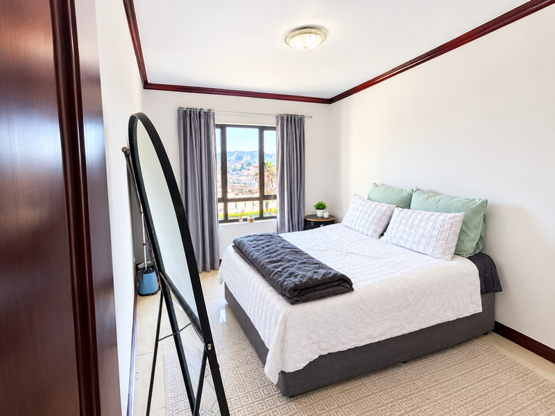 A well-maintained bedroom featuring tiled flooring, dark wood crown molding, and a window with views of the surrounding area.