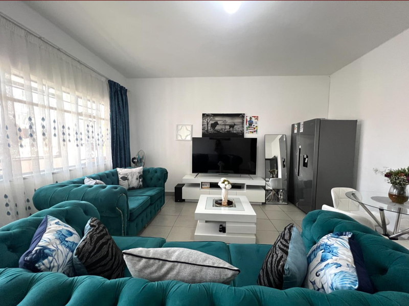A well-maintained living room featuring tiled flooring and a large window with curtain tracks, providing ample natural light.