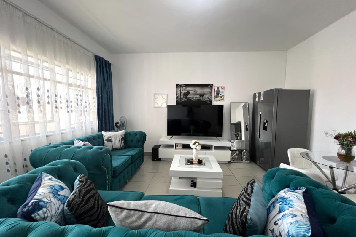 A well-maintained living room featuring tiled flooring and a large window with curtain tracks, providing ample natural light.