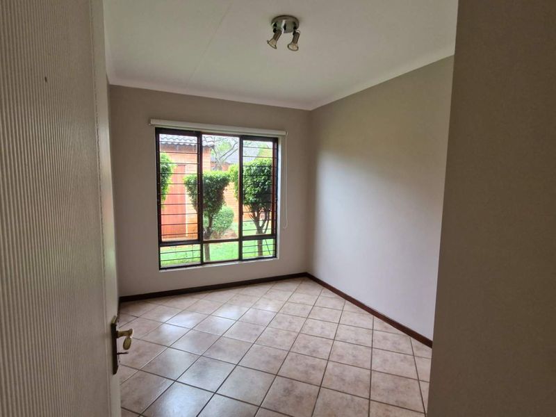 An empty bedroom featuring neutral wall paint, tiled flooring, and a window fitted with security bars, offering a clean and versatile living space.